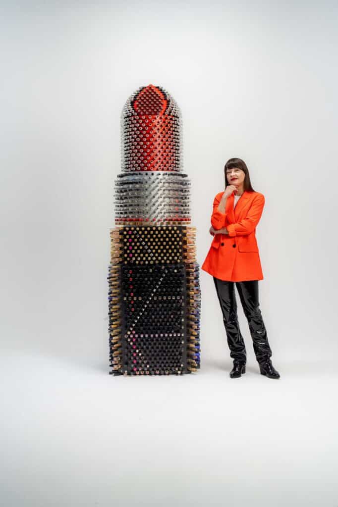 Agne Kišonaitė šalia Lūpdažis milžinas instaliacijos, vilkinti oranžinę aprangą.