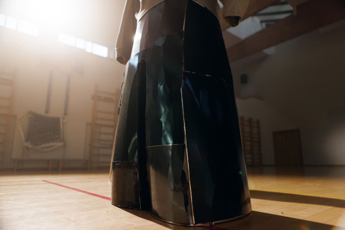 Close-up of a hooded metal figure from the Adolescence art installation by Agne Kisonaite in a school gym.