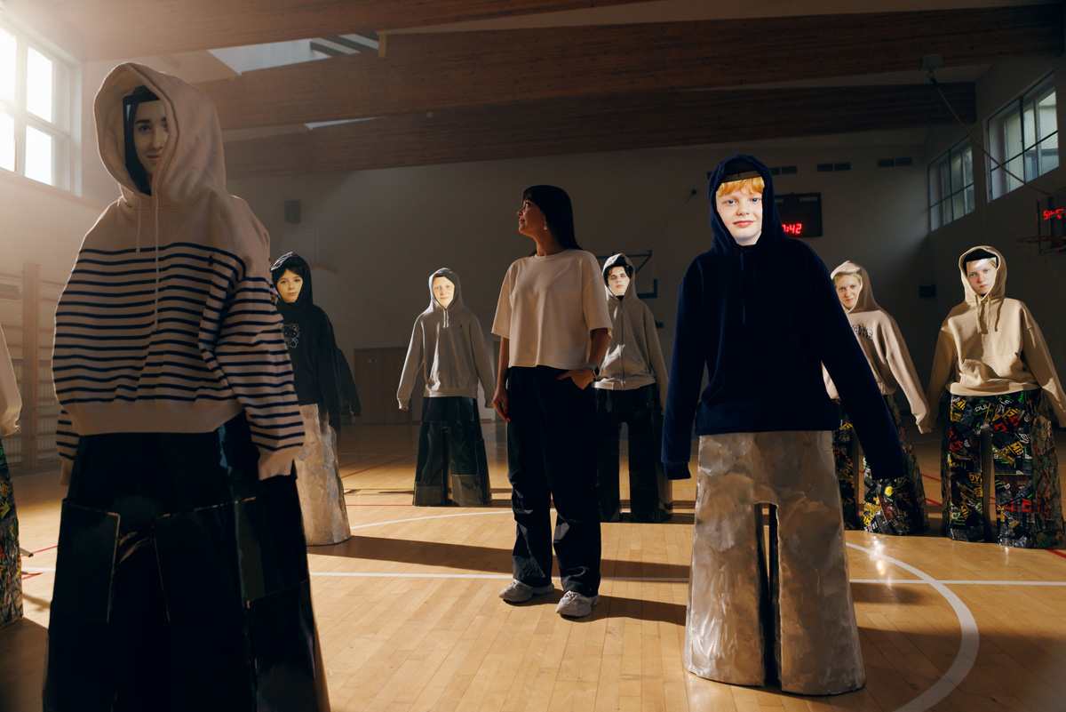 Agne Kisonaite standing among hooded figures from her Adolescence art installation in a school gym